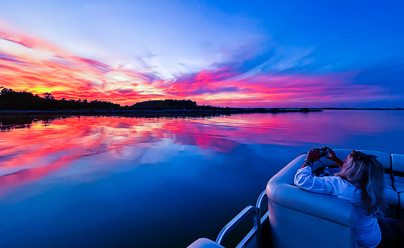 Woman taking a picture of sunset over Grand Lake St Marys from a pontoon boat