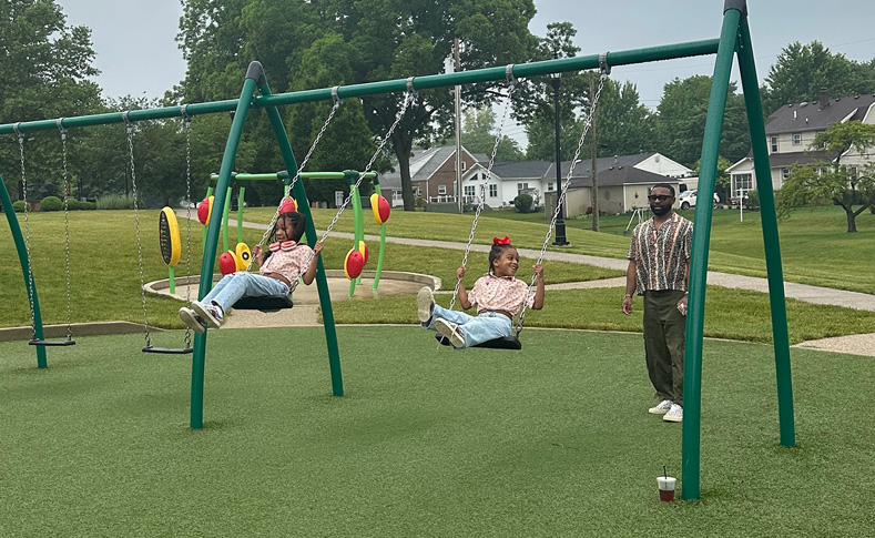 Dad pushing young girls on a swing at komminsk legacy park in New Bremen Ohio